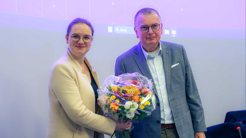 Julia Katharina Eßwein und Prof. Dr. Ory stehen nebeneinander und halten gemeinsam einen bunten Blumenstrauß in den Händen.